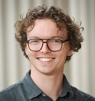 Man with curly hair, glasses, and a green shirt smiles in front of a neutral background.