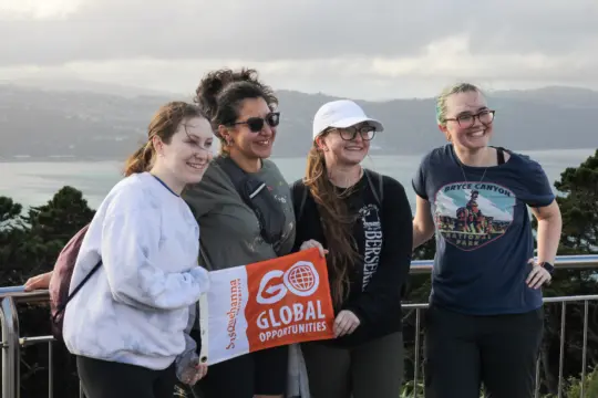 Four students stand together outdoors, smiling and holding a sign reading "Go Global Opportunities."