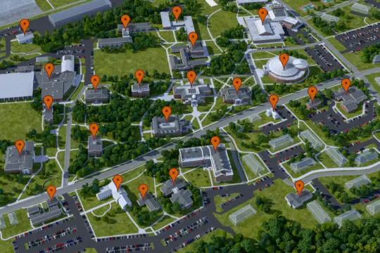 Aerial view of a campus with multiple buildings. Orange location pins are placed on top of various structures. Paths, roads, parking lots, and greenery are visible throughout the scene.