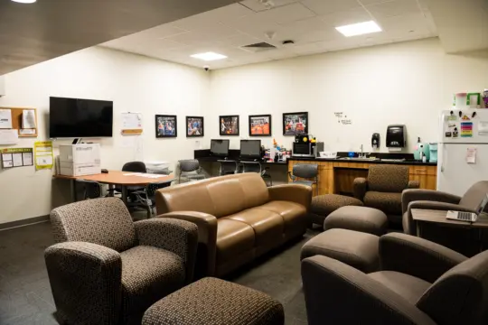 A cozy office lounge welcomes you with cushioned chairs and a sofa, perfect for relaxing between classes. Commuter Student Services provides amenities like a wall-mounted TV, printer, desks with computers, and a corner counter with a coffee maker and microwave for your convenience.