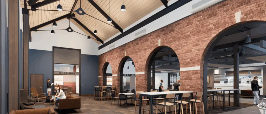 A spacious, modern lounge in Building and Spaces with high vaulted ceilings, brick archways, and large windows. People are sitting and standing, engaging in conversation or working. The atmosphere is bright and welcoming.