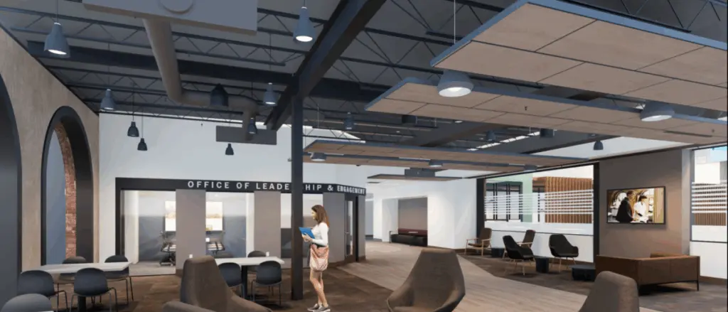Modern office space with open seating, high ceilings, exposed ducts, and large windows. A person stands reading a folder. The area includes tables, lounge chairs, and "OFFICE OF LEADE HIP & EN" sign—showcasing innovative building and spaces design.